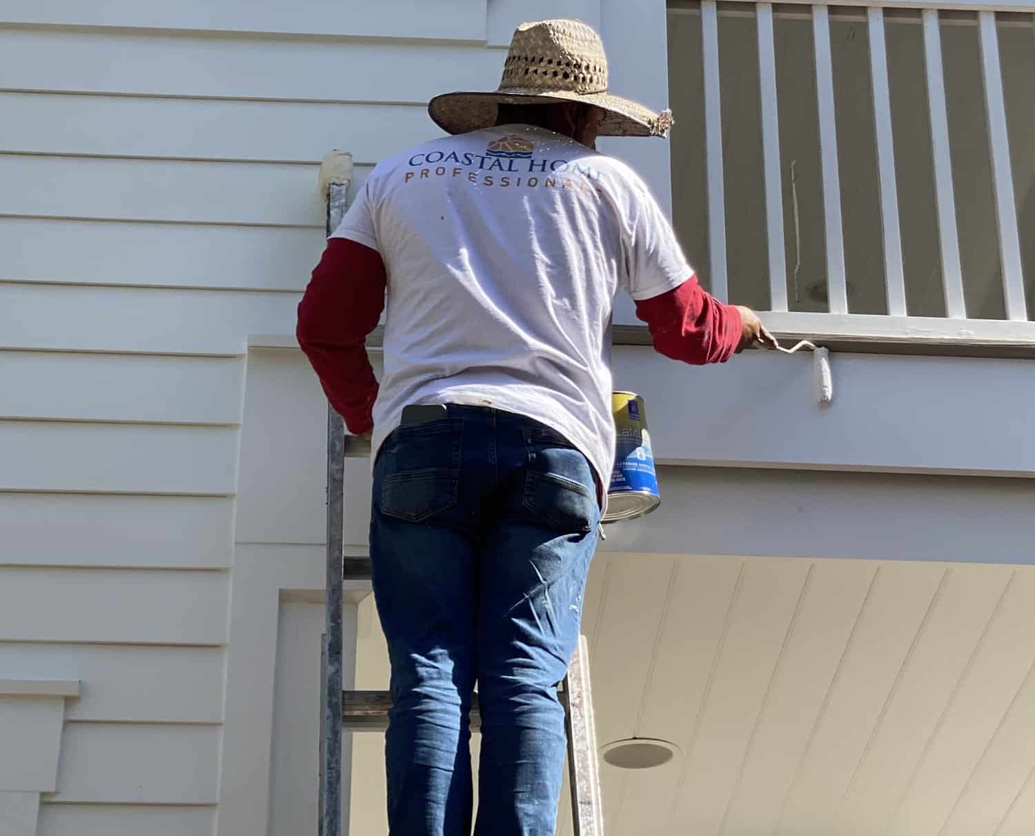 A Custom Home Professional Painter is on a ladder painting the siding of the home
