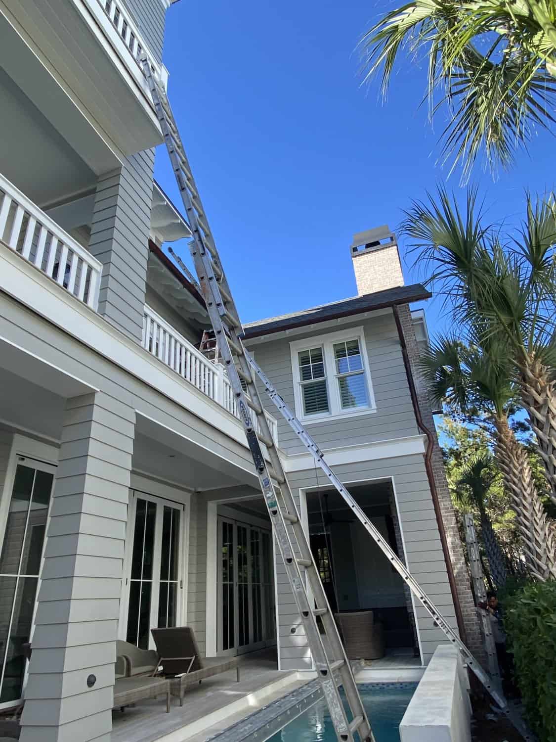 A ladder rests against a 2 story, residential home. Mid painting project