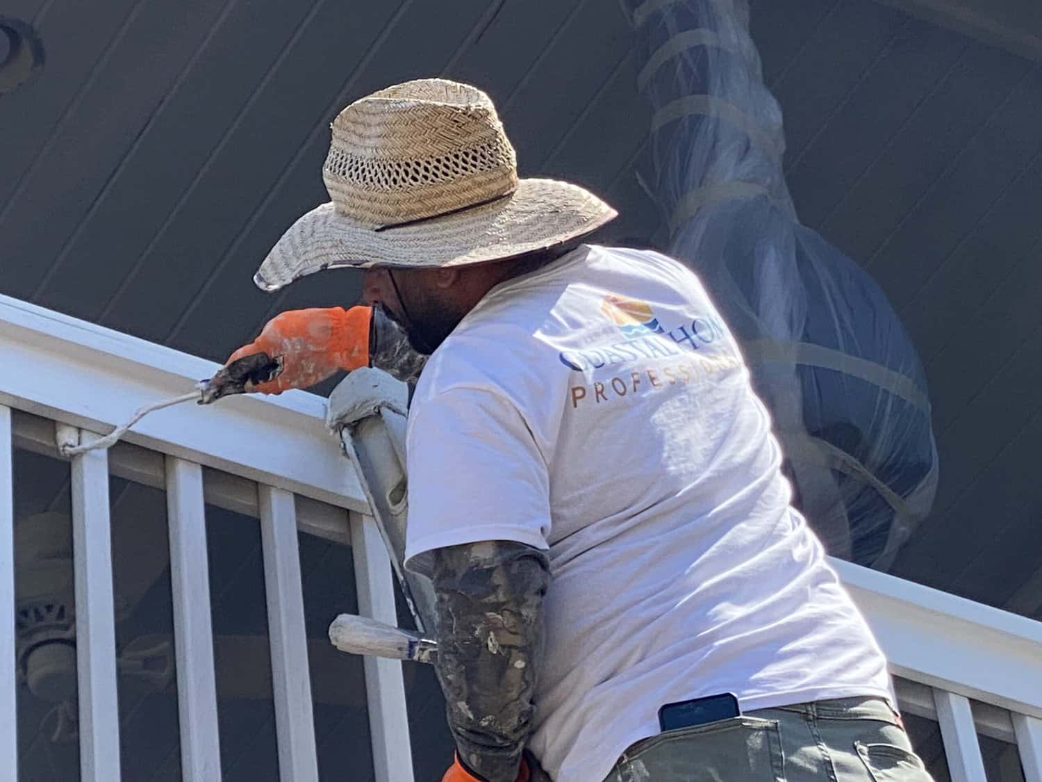 Coastal Home Professional painter is painting the second level deck railing white