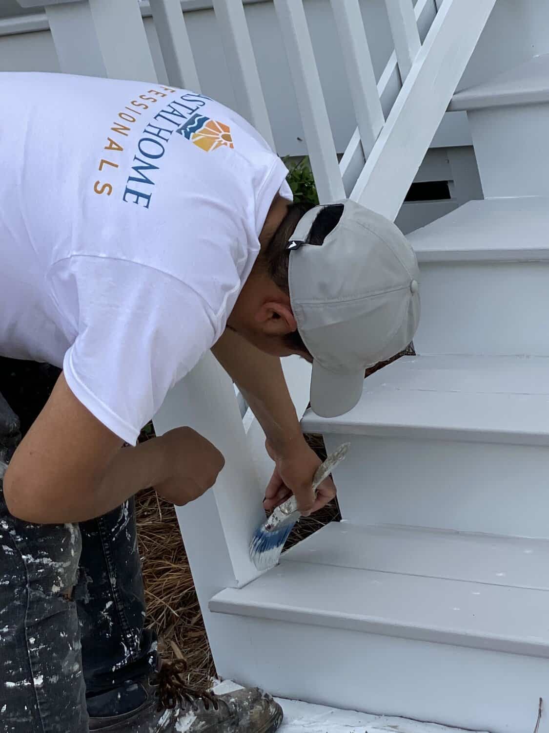 Coastal Home Professional painter is painting a wood railing white.